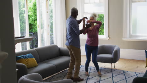 Mixed-race-senior-couple-dancing-together-in-the-living-room-at-home