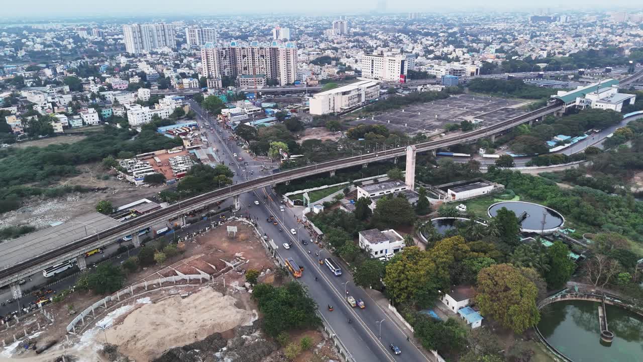 Aerial footage of Chennai with an elevated metro line and a busy road. The scene shows ongoing urban development with a mix of old buildings and new high-rises, perfect for infrastructure themes