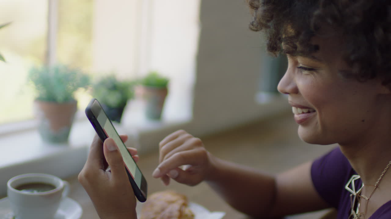 joven mujer afroamericana usando un teléfono inteligente en una cafetería navegando por mensajes en línea bebiendo café elegante mujer negra enviando mensajes de texto compartiendo estilo de vida en las redes sociales disfrutando del teléfono móvil de cerca