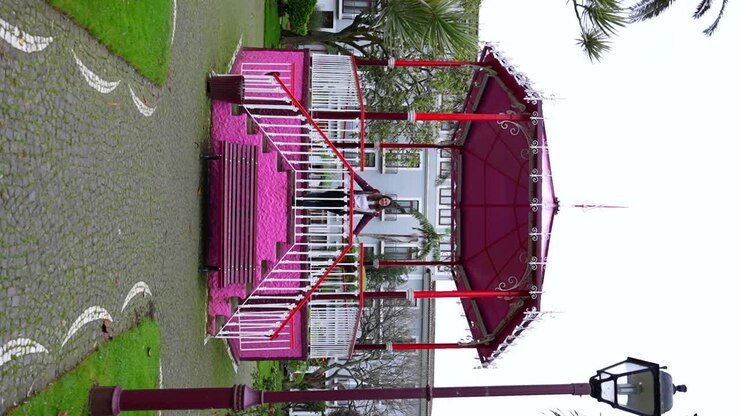 Mulher alegre levantando os braços em um quiosque rosa no Jardim Duque da Terceira, Portugal.