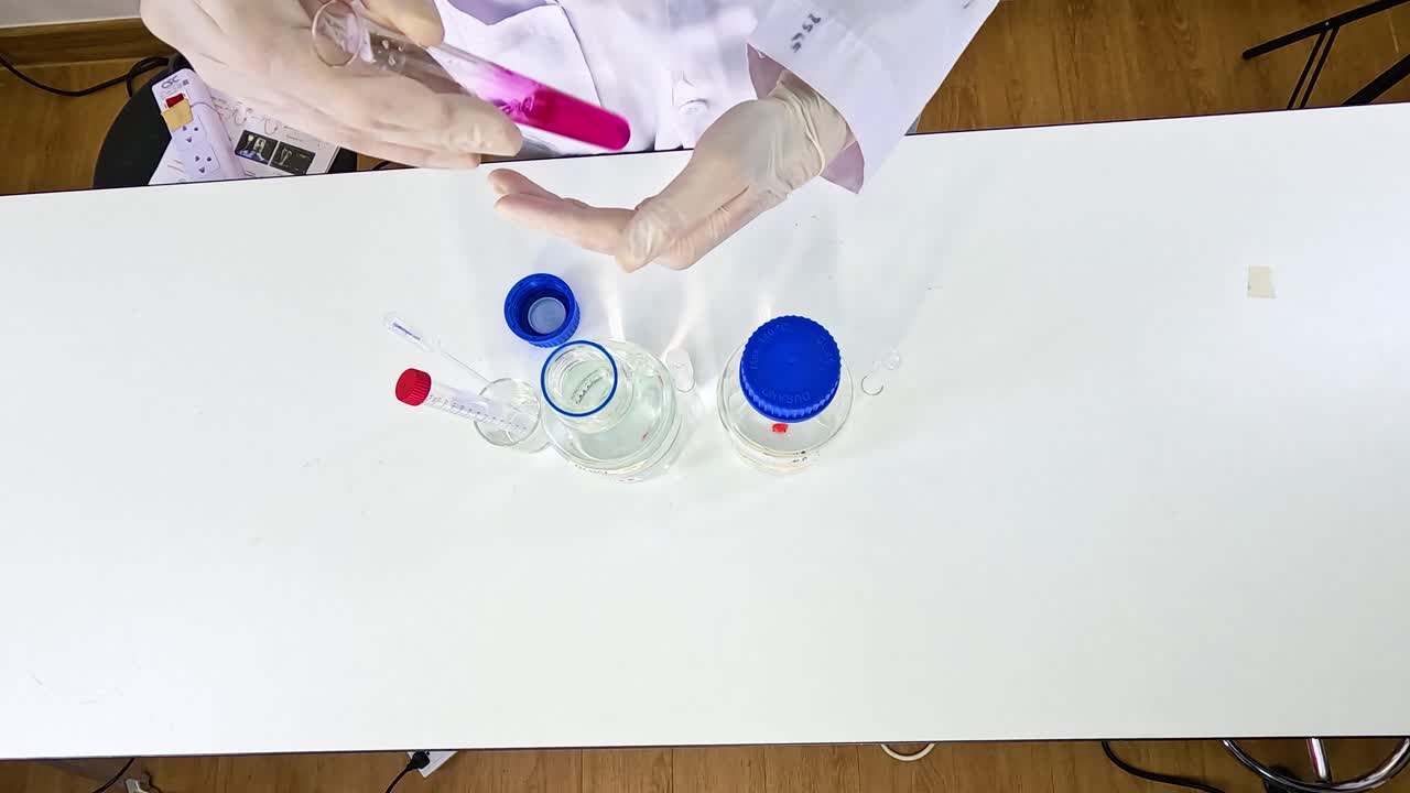Scientist performs a chemical reduction experiment with potassium permanganate using clear glassware on a white table