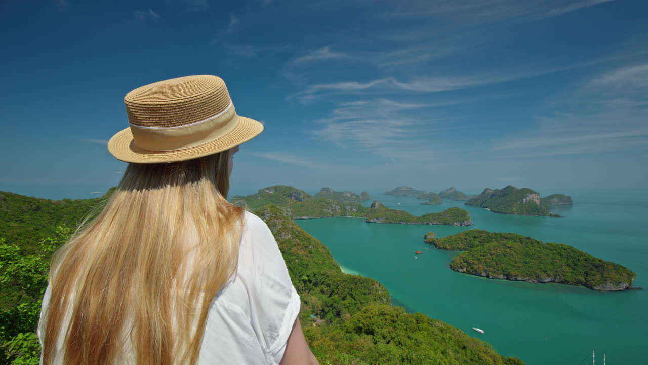 Uma jovem em pé em um mirante panorâmico com vista para uma lagoa esmeralda e ilhas de calcário no Parque Marinho Ang Thong, Tailândia, apreciando a paisagem marinha tropical e as águas azuis e calmas.