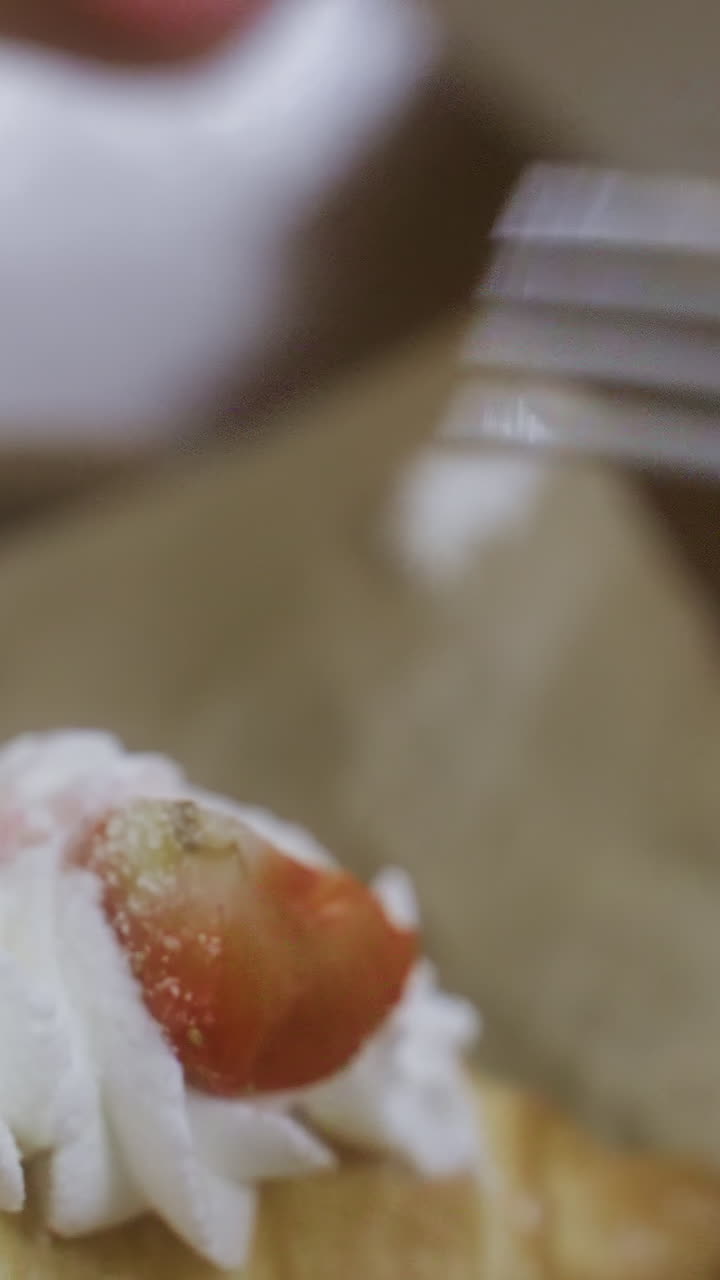 Close-up of female hand unwrapping fork with napkin in cozy cafe, croissant with whipped cream and coffee cup on table. Soft lighting creates relaxed ambiance in background