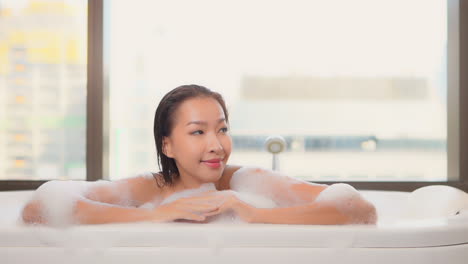 close-up on an asian woman taking bath with foam looking aside and smiling at the hotel resort