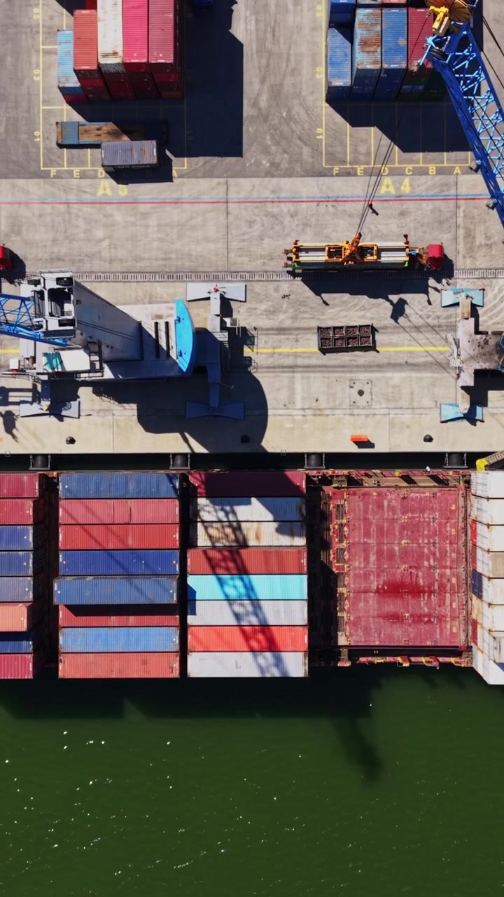 Cargo ship loading containers at a busy port in sunlight