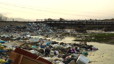 Garbage piled up on river banks, motorbikes pass over bridge, Vietnam