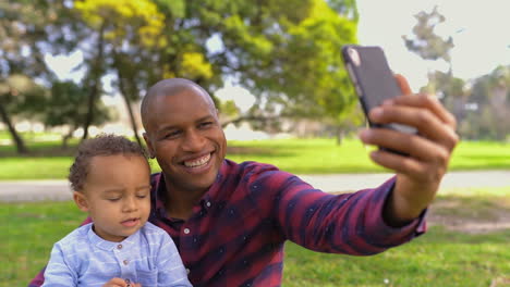 Padre-Haciendo-Selfie-Con-Hijo,-Sonriendo,-Niño-Luciendo-Serio