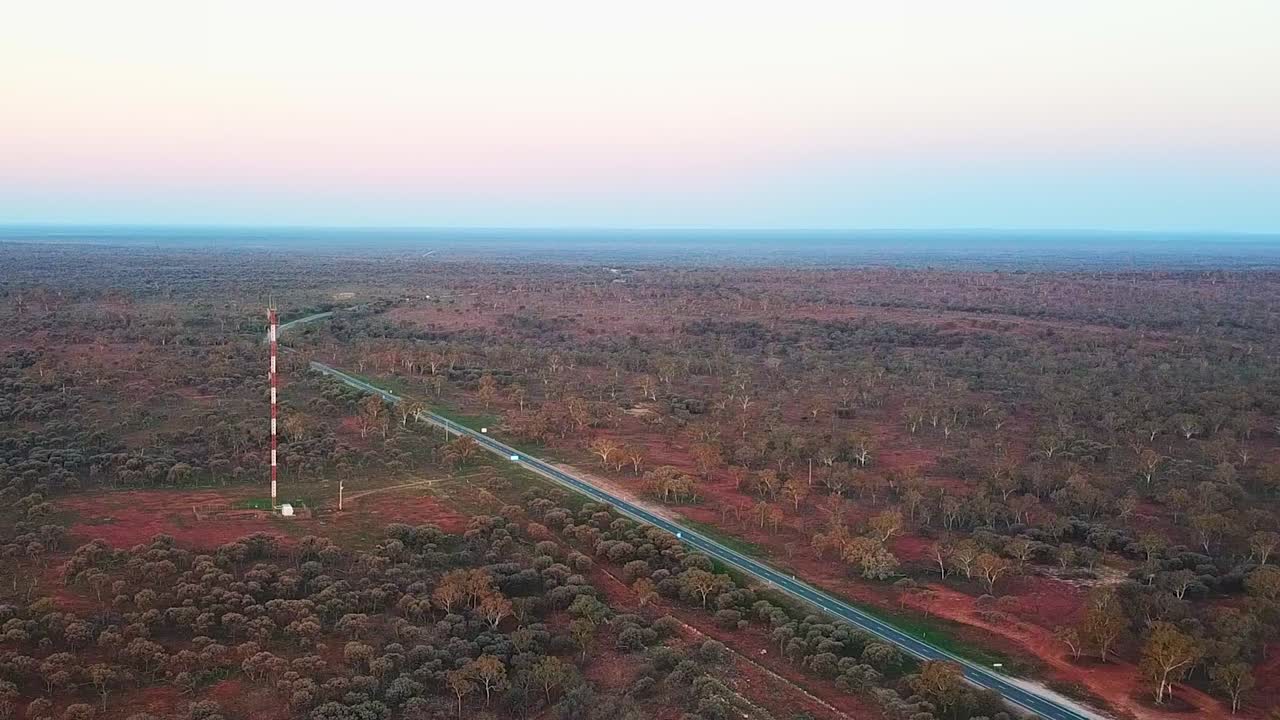 disparo de un dron alto moviéndose hacia una gran torre de comunicaciones y una autopista en el remoto interior de australia