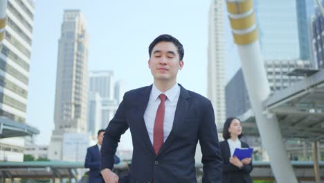 asian young smart businessman using smartphone in city. the man holding phone walking outdoor to working office with smile face. telecommunication and mobile network for business concept.