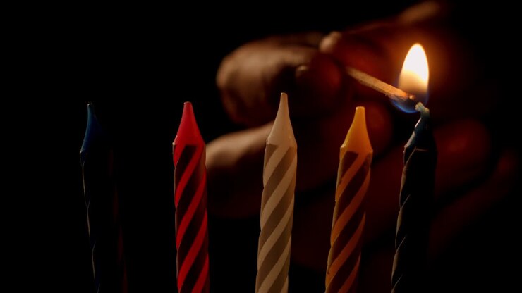 Primo piano: accensione di cinque candeline di compleanno per la torta. Una mano con un fiammifero acceso accende le candeline per la festa di compleanno. Concetto di fuoco vivo, feste e celebrazioni in famiglia.