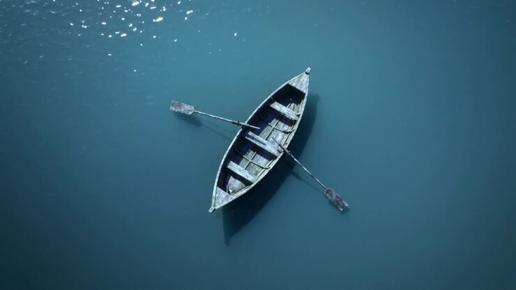 Telecamera che si allontana, barca a remi in legno che va alla deriva su acque calme di un lago, rivelando i riflessi del sole con i remi.