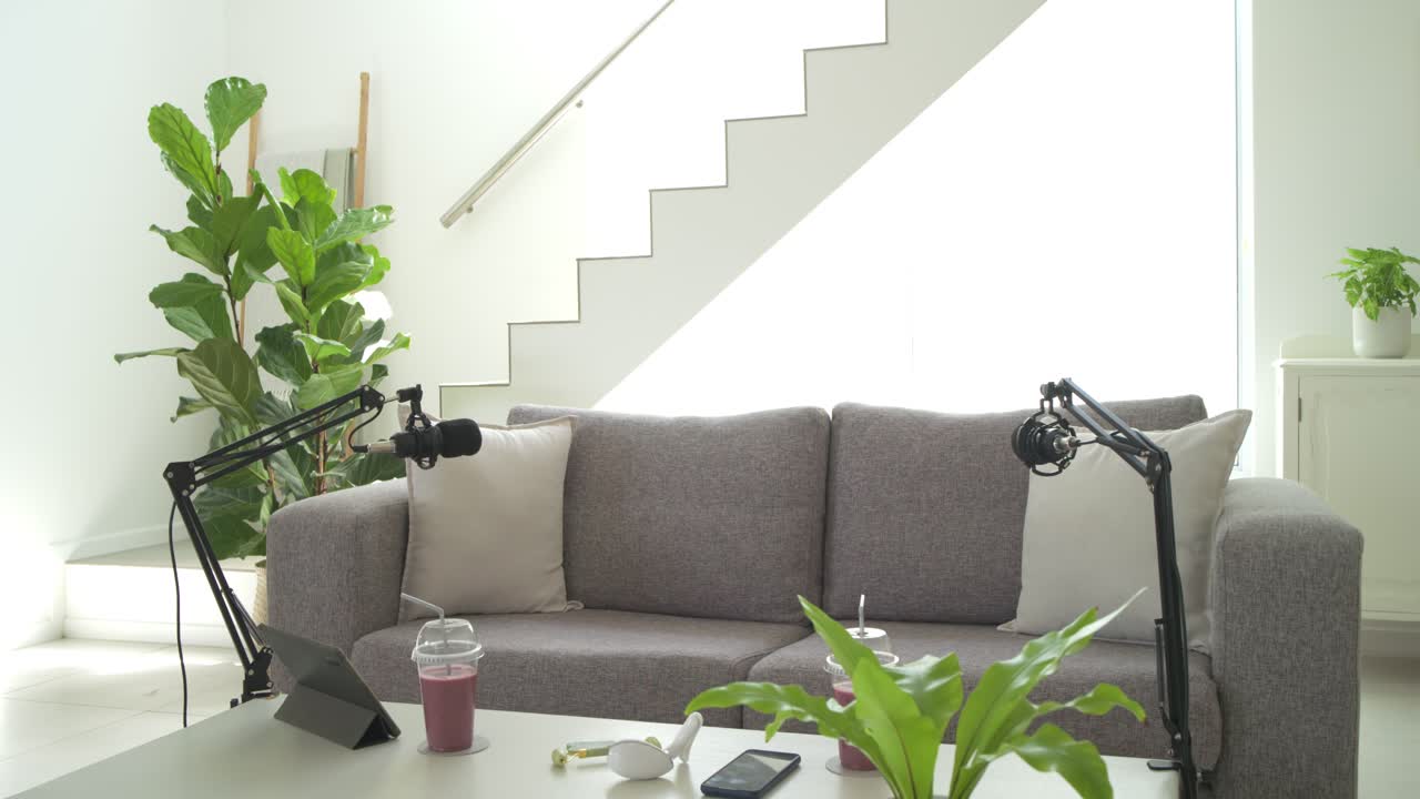 Camera is pulling back to reveal grey sofa and podcast setup as mic arms are adjusting