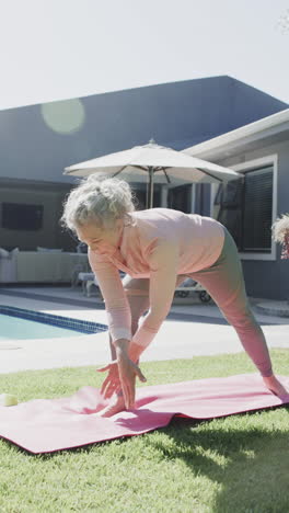 vertical video of happy senior caucasian woman doing yoga, stretching in garden, slow motion