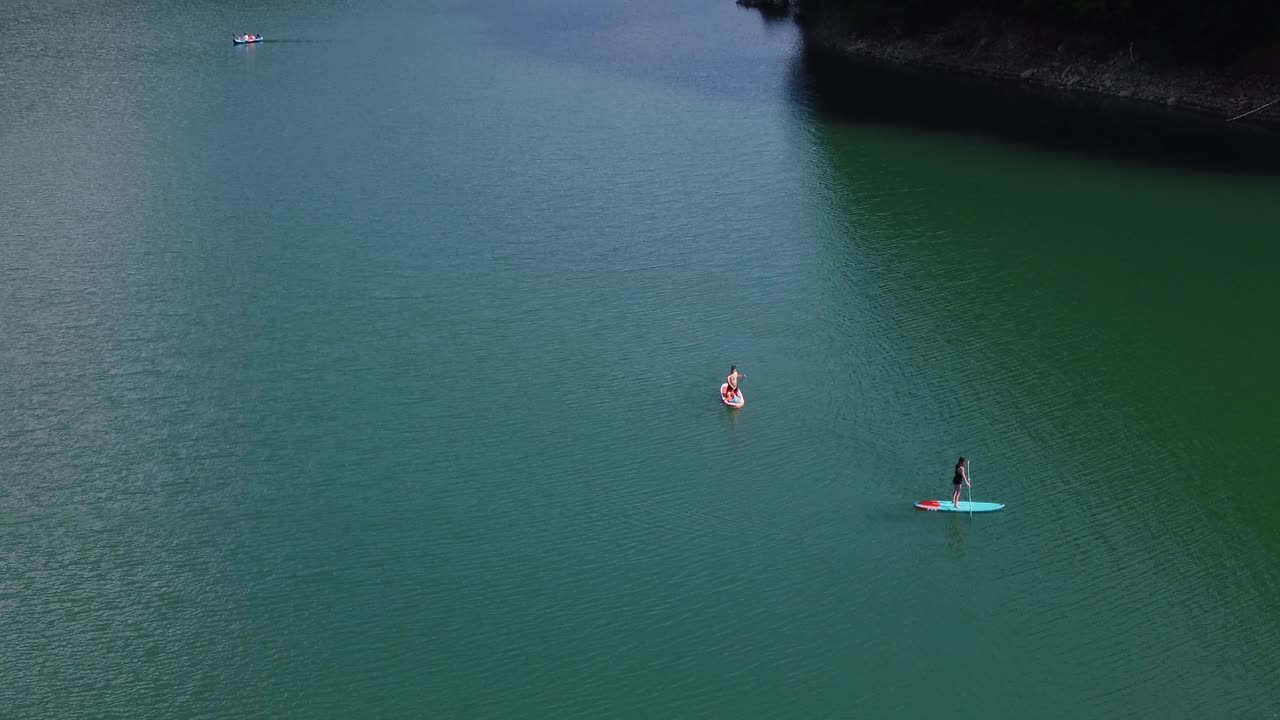Aerial shot of young couple having a relaxing afternoon on paddle boards on  Paltinu lake of Doftana Valley in Romania
