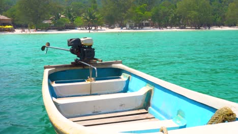 small-empty-boat-rocking-with-the-waves,-tied-up-near-beautiful-beach,-cambodia