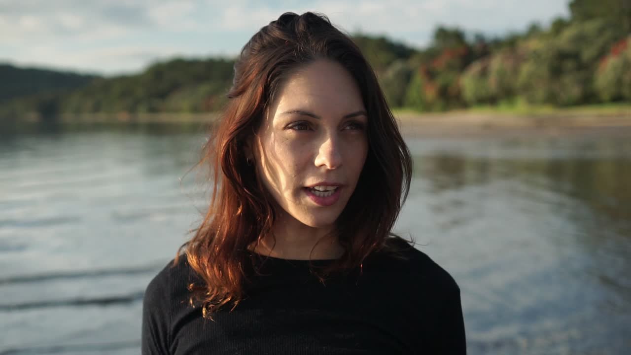 Portræt af kvinde, der rører ved håret på stranden, ansigt i nærbillede forfra i slowmotion
