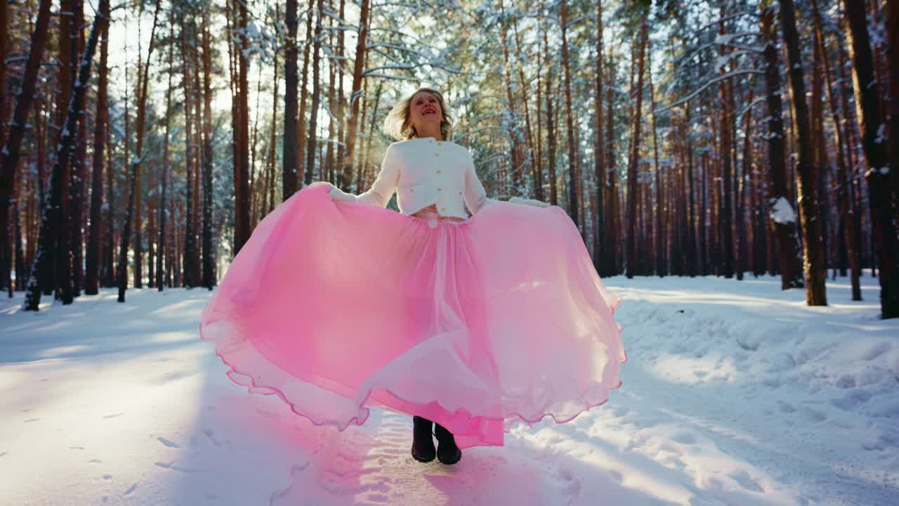Donna gioiosa che volteggia con una gonna rosa in una foresta invernale innevata.