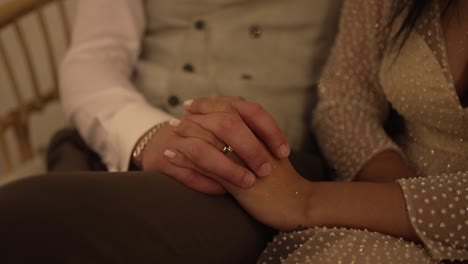 una pareja tomándose de la mano, compartiendo un momento íntimo, con un primer plano de sus anillos de bodas