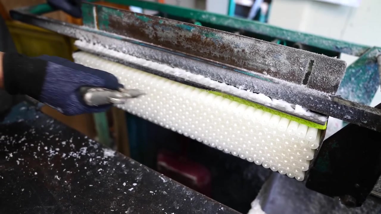 Worker adjusting a textured wax roller mold with a gloved hand at a candle factory
