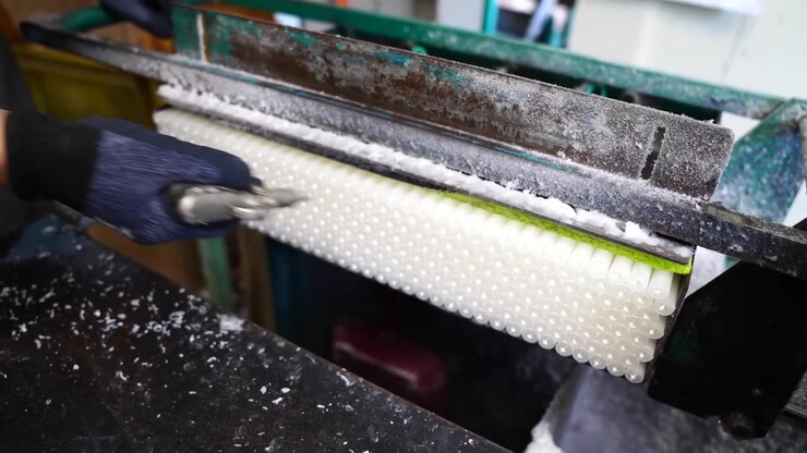 Worker adjusting a textured wax roller mold with a gloved hand at a candle factory