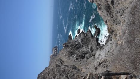 Vertical-shot-of-Punta-Lobos,-waves-crashing-against-rocky-sea-cliffs-in-the-middle-of-the-day-near-Todos-Santos,-BCS,-Mexico