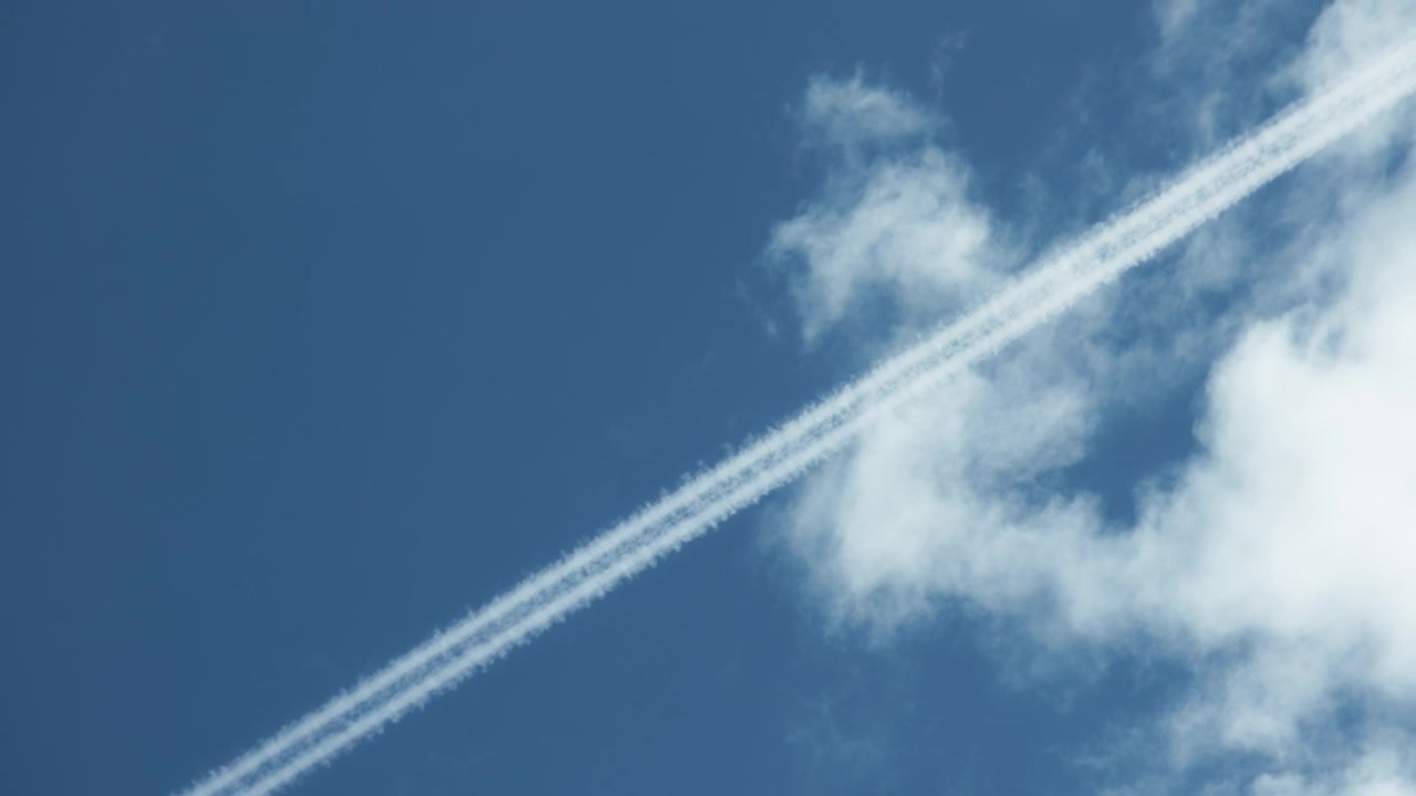Kondensstriber efterladt af et fly på en blå himmel med hvide skyer