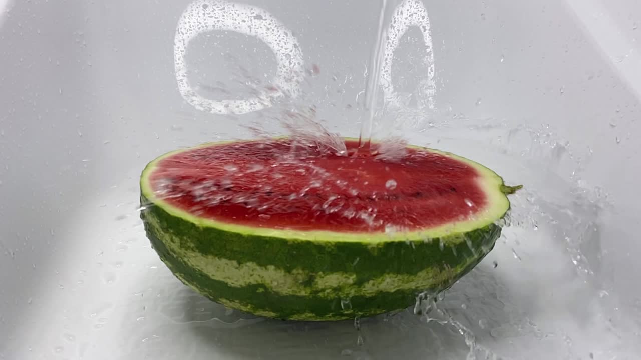 물의 제트가 잔한 은 익은 수박에 떨어지고 반으로 잘라서 스프레이를 떨어뜨립니다.