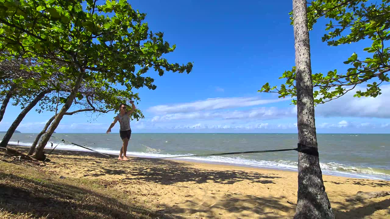 macho adulto joven subiendo a slackline y caminando en trinity beach en cairns