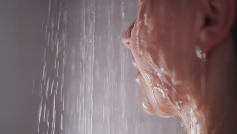 water runs down face of young woman in shower. lady with earnings takes pleasant shower. woman stands in shower feeling water flows down along face