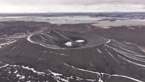 Aerial view of the volcanic crater Hverfjall near Lake Mývatn, Iceland, showcasing the symmetrical caldera partially covered in snow.