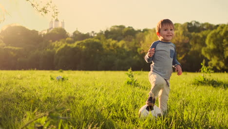 In-slow-motion-a-happy-boy-with-a-soccer-ball-runs-into-the-field-at-sunset-dreaming-of-playing-professional-football.