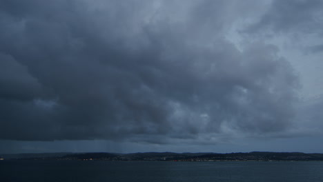 Heavy-clouds-and-rain-passing-over-seaside-town-and-water,-timelapse