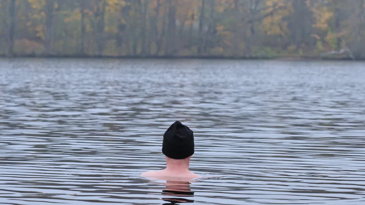 Focused man practices cold immersion therapy in icy lake under autumn trees