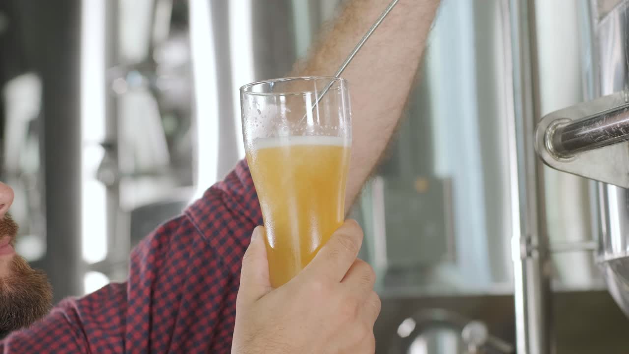 un joven cervecero con un delantal de cuero está probando cerveza en una cervecería moderna