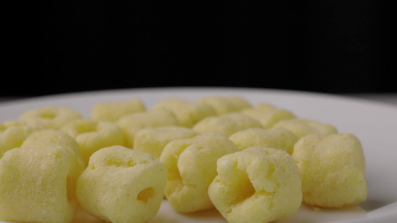 Primo piano di snack croccanti di anelli di mais salati che ruotano lentamente. Concetto di snack fast food o cibo spazzatura non salutare