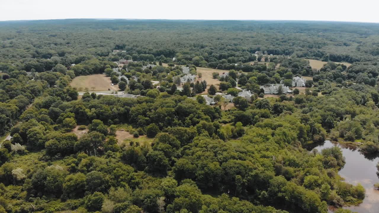 Descending drone shot of a forest around a small town in Massachusetts with a cloudy sky overhead - 4K