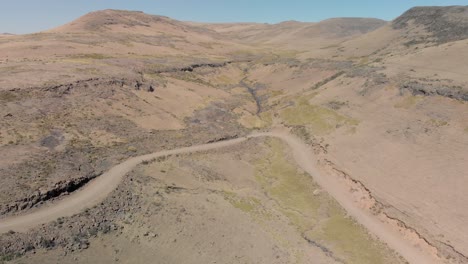 Toma-Aérea-Siguiendo-A-Dos-Ciclistas-De-Montaña-Subiendo-Un-Paso-De-Montaña-De-Camino-De-Ripio