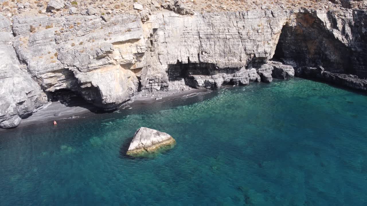 4k video drone footage of a breath taking view of a turquoise beach under rocky cliffs during a sunny day