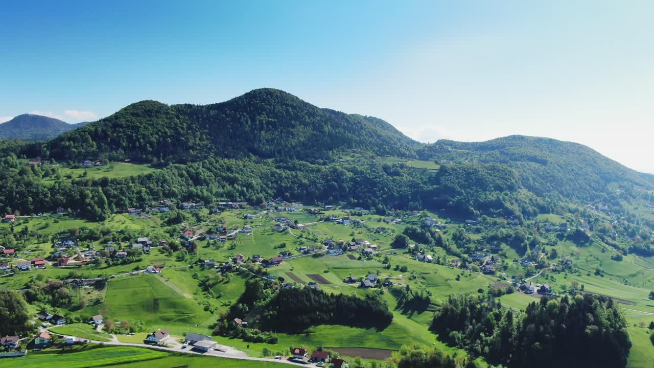 Aerial Over Village Town Nestled At Foothill Of Forested Hill