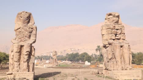 Ruinen-Der-Beiden-Riesigen-Statuen-Des-Pharaos-Mit-Bergen-Im-Hintergrund-Bei-Den-Kolosse-Von-Memnon-In-Luxor,-Ägypten