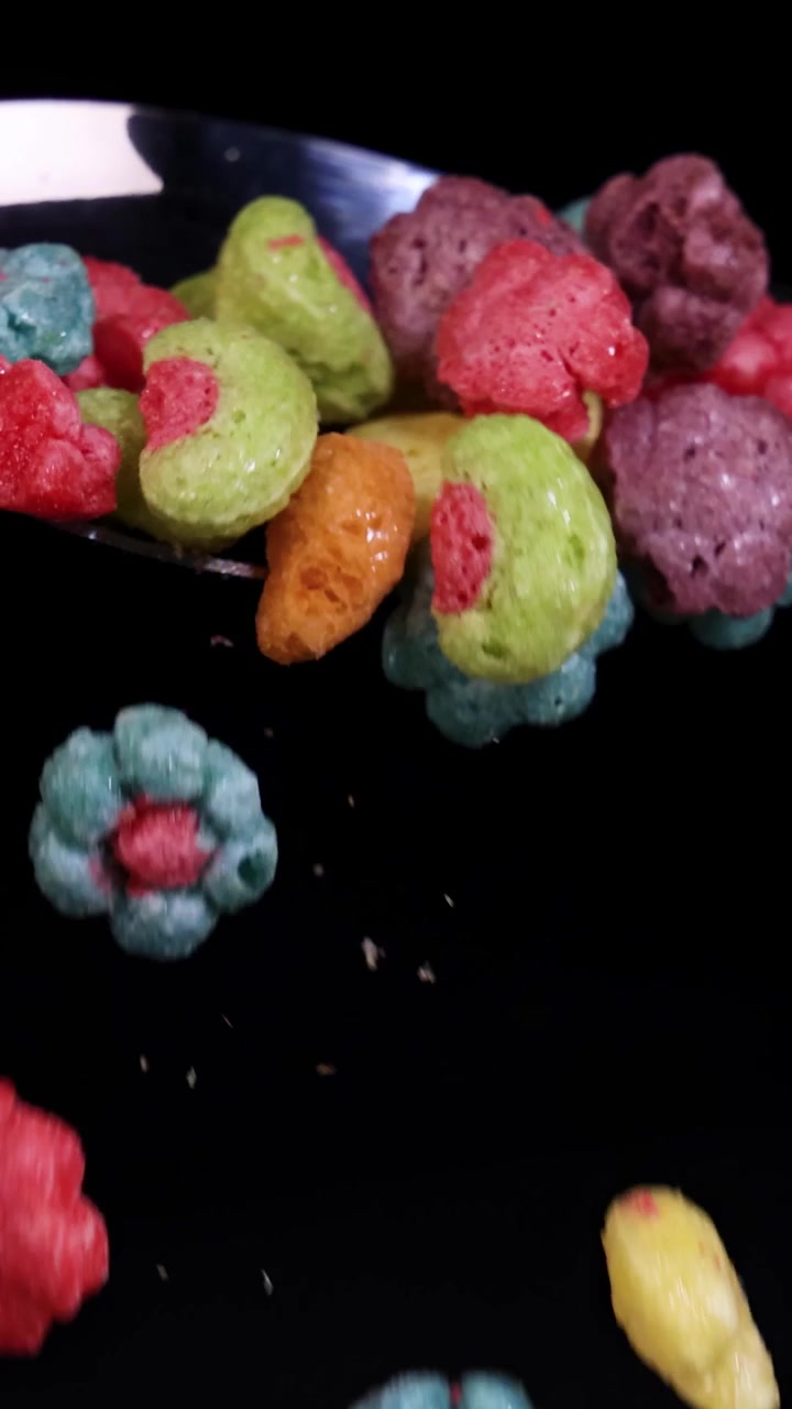 Cereais coloridos caindo de uma colher contra um fundo preto, capturados em câmera lenta com iluminação dramática.