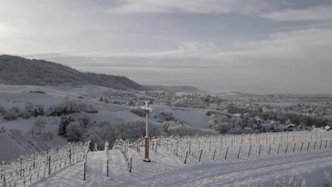 Drone-Orbitando-En-Cruz-Situado-En-Un-Viñedo-Nevado-Con-Enrejado-Cerca-De-Zell-weierbach-En-Offenburg,-Alemania