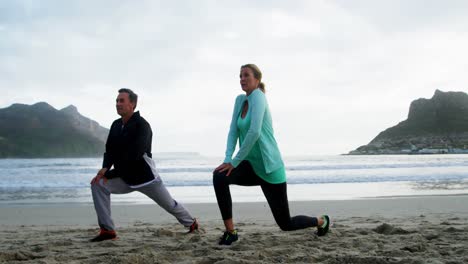 mature couple performing stretching exercise on beach