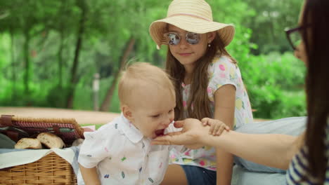 Mother-giving-cherry-to-boy-at-picnic.-Happy-toddler-eating-cherry