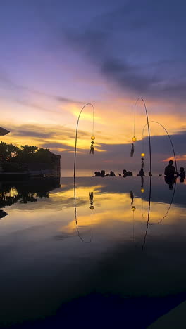 vertical view, purple sunset sky reflection on pool water of tropical resort and silhouettes of people