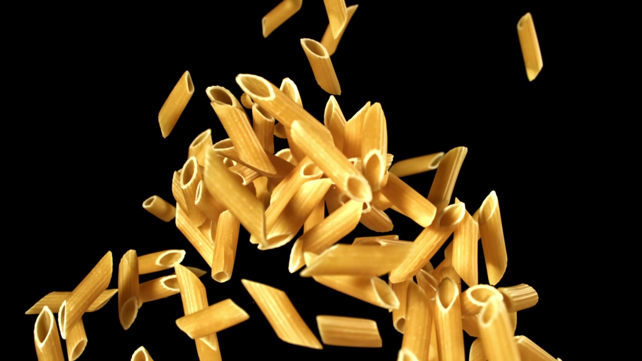 Pasta penne secca che cade e si accumula su sfondo nero