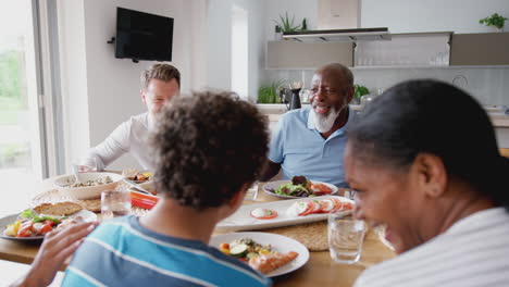 Familia-De-Raza-Mixta-Multigeneracional-Comiendo-Comida-Alrededor-De-La-Mesa-En-Casa-Juntos