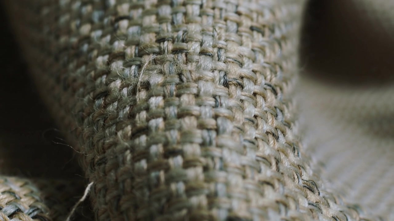 Shifting camera focus revealing coarse woven textile in studio, highlighting stray fiber and fold
