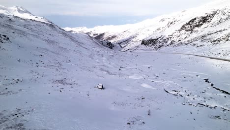 Aerial-back-view-of-a-man-in-a-red-jacket-looking-at-a-snow-covered-mountain-pass-on-a-winter-day-in-Fluela-Pass,-Switzerland