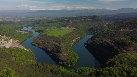 a winding river in salvassola vic near barcelona, lush greenery and mountainous backdrop, aerial view